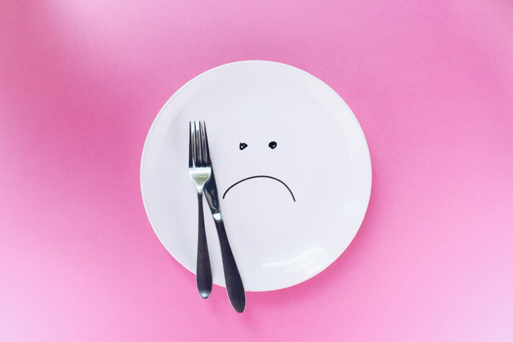 Plate with sad face drawing, fork, and knife on pink background.